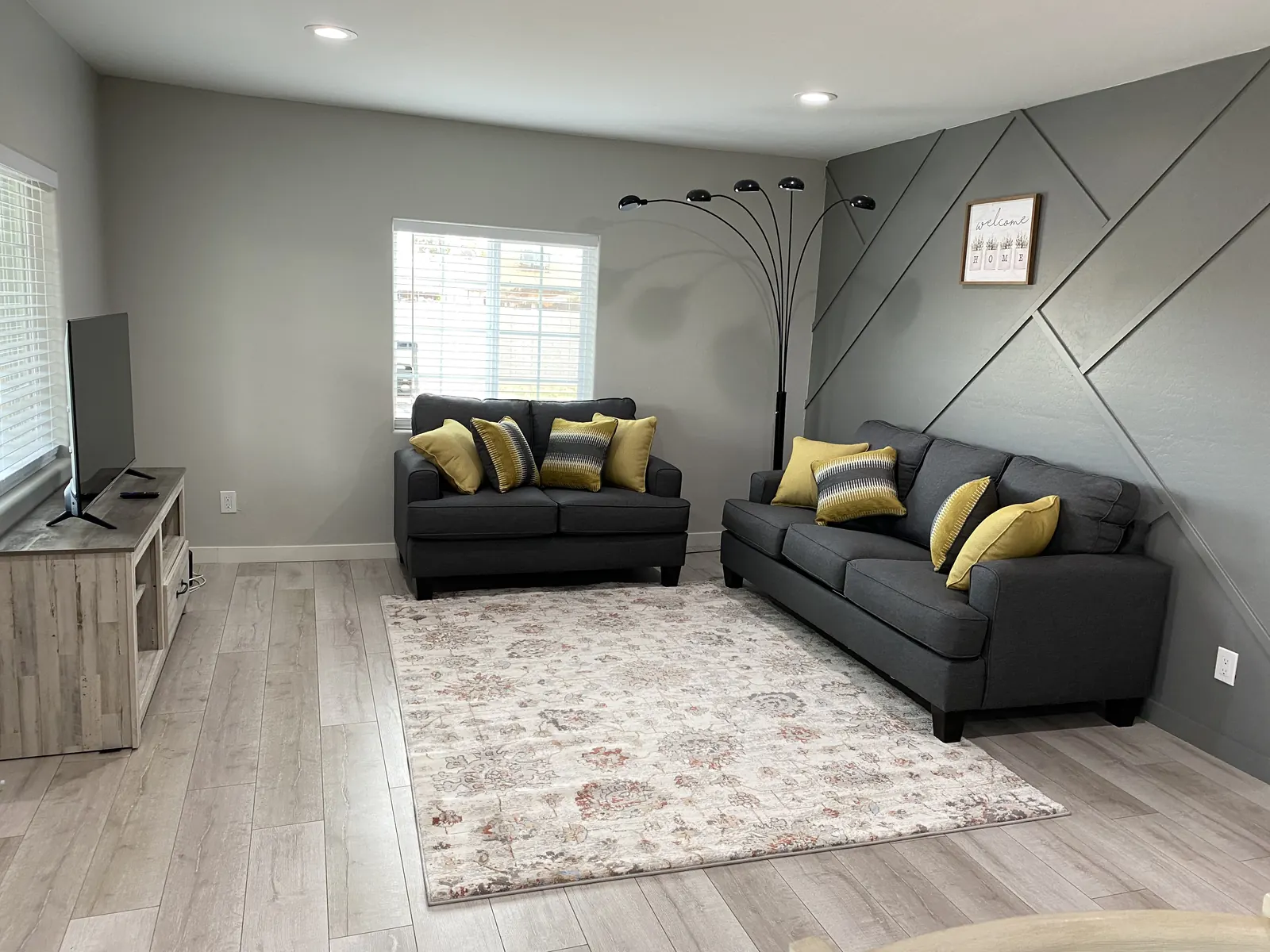 Living room with a dark panelled accent wall and two grey sofas in a Roadmap Lodging home in Avondale, Arizona